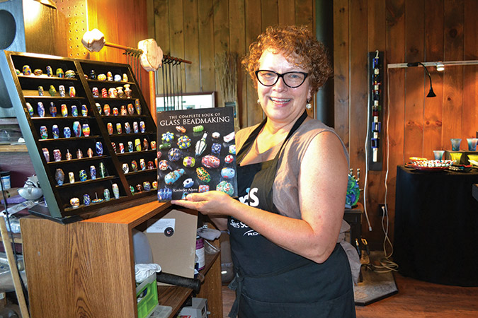 Kimberley Adams, glass artist, proudly holds the book she wrote about glass beadmaking—a definitive guide that is a respected source on the subject.