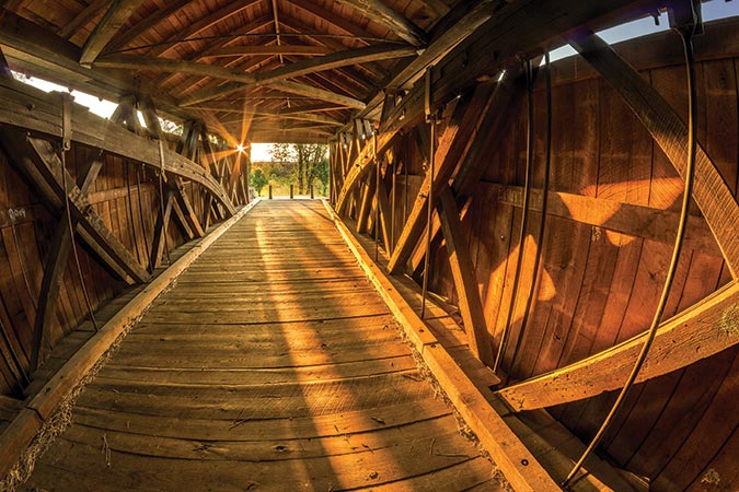 The low setting sun shines through the wooden beams of the Mud River covered bridge in Milton, West Virginia. The bridge that once spanned the Mud River in the mid 1800s has now been restored and relocated to Pumpkin Park in Milton and placed on the National Register of Historic Places.