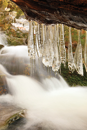 This image was captured along the Jones River Trail in Shenandoah National Park, Virginia, where a log crosses the river and icicles have grown as water from the cascade splashes onto the log.