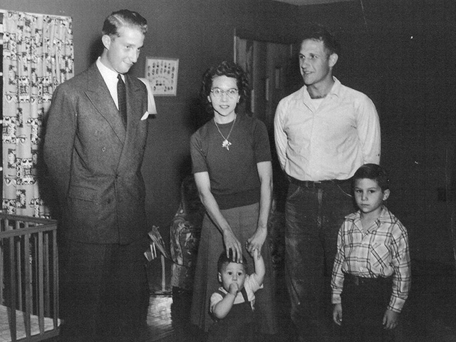 Prince Albert of Belgium stands in the home of dairyman Ralph Peterson and his wife Hazel in rural East Tennessee in 1955. Dale Peterson (far right) and writer Dennis Peterson—content with his thumb—stand by, oblivious to the significance of their unexpected visitor.
