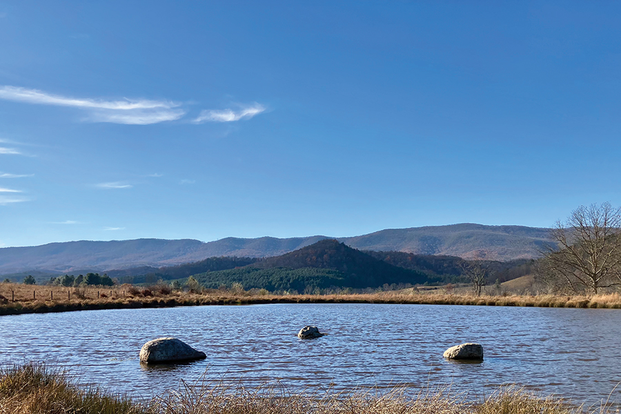 The view of Bear Pond from the trail features three serene rocks and a long view of the surrounding mountains.