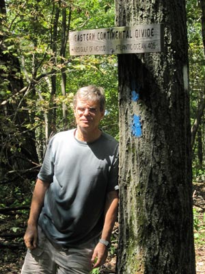 This man is: A. Contemplating the walking distances on the sign. B. Reflecting the mood of the photographer. C. Just old, cranky and squinty-eyed.