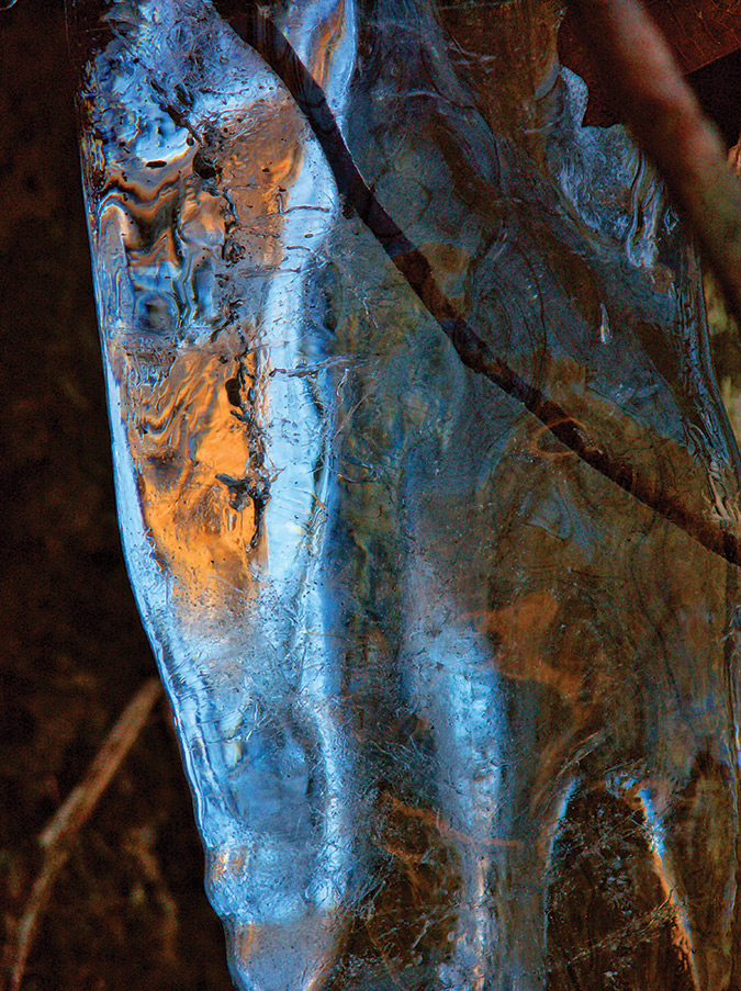 The blues and golds of winter are eerily refracted in this icicle from Blue Hole Falls, West Virginia. The ice bends the shades of blue light from the sky and brown light from the hillsides. The effect is a stunning kaleidoscope of color.