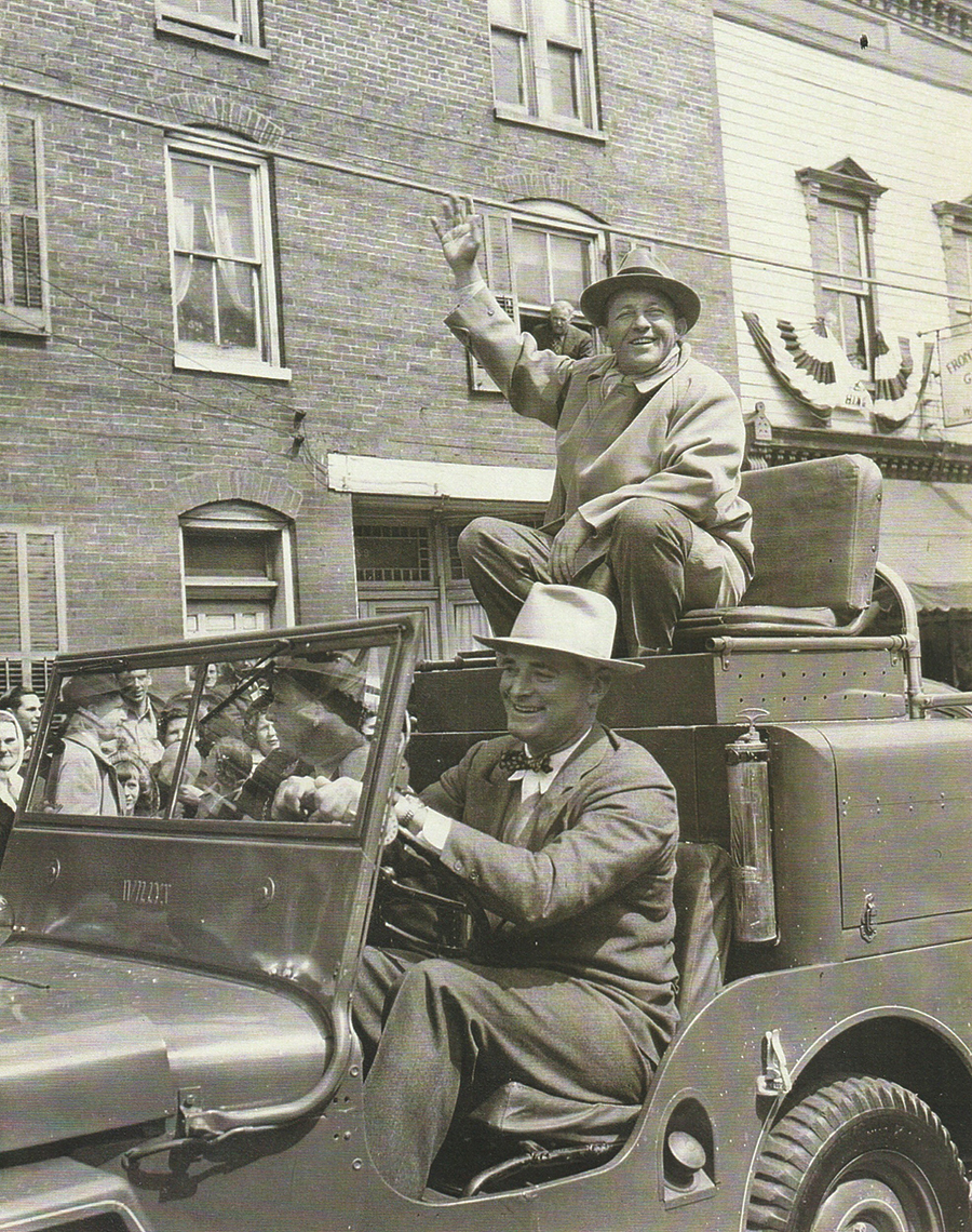 Bing Crosby waves to crowds along the parade route, escorted by his friend, Virginia Senator Raymond R. Guest, Sr.