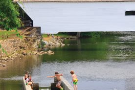 Children cool off on a hot summer day by jumping into the fish ladder of the weir dam on the Doe River just downstream of the Elizabethton Covered Bridge in Elizabethton, Tennessee.