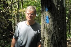 This man is: A. Contemplating the walking distances on the sign. B. Reflecting the mood of the photographer. C. Just old, cranky and squinty-eyed.