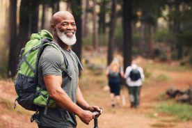 Man hiking in forest, exercise and fitness for wellness, healthy lifestyle and smile. Face, senior male and mature gentleman with backpack, smile and hiker in woods and fresh air.